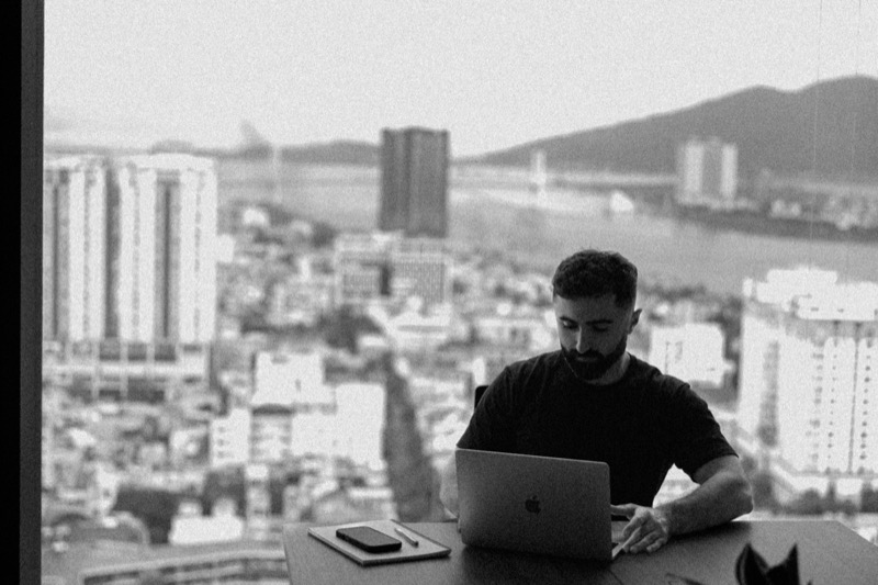 Black-and-white photo of a man working at a laptop in front of a city skyline