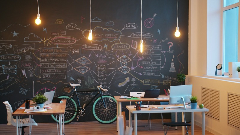 A bright creative office with a chalkboard wall covered in planning notes, desks, and a bicycle