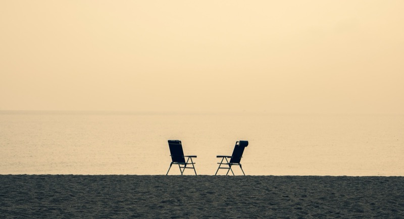 Two empty beach chairs side by side on sand, facing calm water at dusk