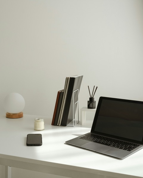 A minimalist white desk with a laptop, notebooks, and a small lamp set up for a video therapy session