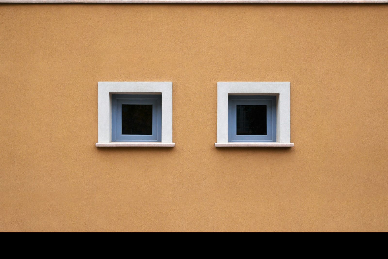 Two identical square windows set into a warm ochre wall