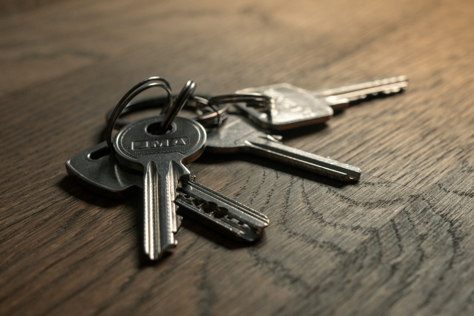 A ring of three worn metal keys lying on a dark oak tabletop, lit from one side