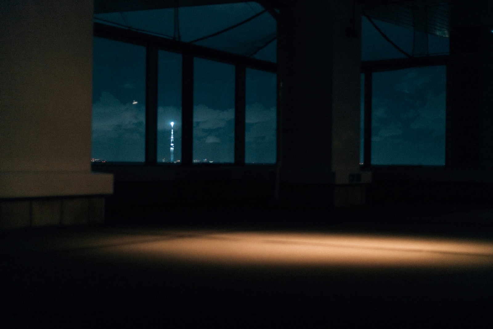An empty office at night, a lit tower in the distance through the windows and a patch of warm light on the floor